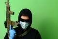 Criminal in a medical surgical mask and sunglasses dressed in black with a hood holds an automatic assault weapon Royalty Free Stock Photo