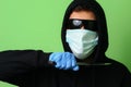 Criminal in a medical surgical mask and sunglasses dressed in black with a hood holds a knife in his hand Royalty Free Stock Photo