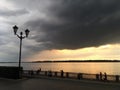 Crimson orange sunset on the river, dark clouds over the city`s waterfront