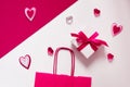 On a crimson and white background, a gift box with a pink bow, a pink paper shopping bag, crimson glass hearts hearts Royalty Free Stock Photo