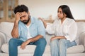 Crisis in marriage, divorce, breakup. Loving indian woman talking and touching her indifferent husband, sitting on couch Royalty Free Stock Photo