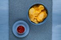 Crisps in a blue bowl with ketchup on a light blue background, top view, space for text.Convenient snack concept