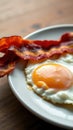 Crispy bacon strips accompanied by a perfectly cooked sunny-side-up egg on a white plate Royalty Free Stock Photo