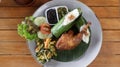 Crispy black fried duck with rice covered in banana leaf, some veggetable and special mash chili