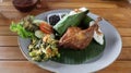 Crispy black fried duck with rice covered in banana leaf, some vegetable and special mash chili