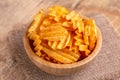Crispy corrugated potato chips in wooden bowl on burlap napkin