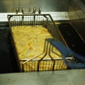 Crispy french fries in a deep fat fryer with steel net basket Royalty Free Stock Photo