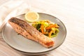 Crispy fried salmon fillet with leek and carrot vegetable and la lemon slice on a plate, light wooden table with copy space Royalty Free Stock Photo