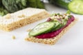 Crispy low-calorie wheat crackers with beet hummus, pine nuts and cucumbers on a background of greens on a white wooden table. Royalty Free Stock Photo