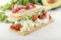 Crispy low-calorie wheat crackers with curd cheese and sun-dried tomatoes on a background of avocado and greens on a white wooden Royalty Free Stock Photo