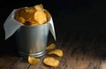 Crispy potato chips in a small zinc bucket on a rustic wooden floor.