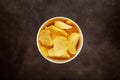 Crispy potato chips in a white bowl on textured brown background Royalty Free Stock Photo
