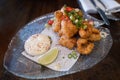 Crispy squid garnished with salad served with a mayonnaise dip on a glass plate and wooden table