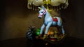 Cristmas presents. A toy, a white rocking horse, small gifts, a green ball, a pine cone. Night light. Zone light on gold fabric.