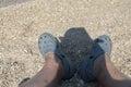 Croatian pebble beach with legs and reflection of man with hat. Royalty Free Stock Photo