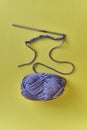 Crochet hook, chain of loops made of violet threads and skein of acrylic yarn on yellow background.