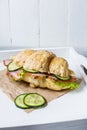 Croissant with cheese, ham, cucumber and salad on white tray