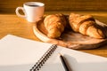 Croissant with coffee cup, notebook and pencil on wooden table background. Royalty Free Stock Photo