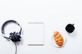 Croissant, coffee, headphones and notebook on white table