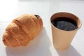 Croissant and coffee to go in brown craft paper cup on white background. Royalty Free Stock Photo