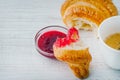Croissant dipped in berry jam with cup of coffee