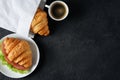 Croissant with ham and lettuce, coffee on a dark background.