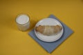 Croissant on a plate on a blue napkin and a glass of milk on yellow background flat lay