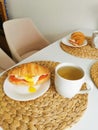 Croissant with poached egg and tomatoes with tea in the kitchen. Delicious breakfast in the white kitchen. Royalty Free Stock Photo