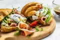 Croissant with prosciutto, poached egg, jamon, blue, cheese, avocado, microgin and cherry tomatoes. Mediterranean appetizer.