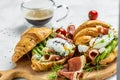 Croissant with prosciutto, poached egg, jamon, blue, cheese, avocado, microgin and cherry tomatoes. Mediterranean appetizer.