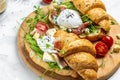 Croissant with prosciutto, poached egg, jamon, blue, cheese, avocado, microgin and cherry tomatoes. Mediterranean appetizer.