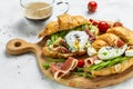 Croissant with prosciutto, poached egg, jamon, blue, cheese, avocado, microgin and cherry tomatoes. Mediterranean appetizer.