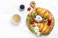 Croissant with prosciutto, poached egg, jamon, blue, cheese, avocado, microgin and cherry tomatoes. Mediterranean appetizer.