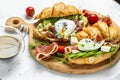 Croissant with prosciutto, poached egg, jamon, blue, cheese, avocado, microgin and cherry tomatoes. Mediterranean appetizer.