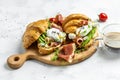 Croissant with prosciutto, poached egg, jamon, blue, cheese, avocado, microgin and cherry tomatoes. Mediterranean appetizer.