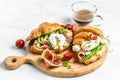 Croissant with prosciutto, poached egg, jamon, blue, cheese, avocado, microgin and cherry tomatoes. Mediterranean appetizer.