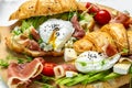 Croissant with prosciutto, poached egg, jamon, blue, cheese, avocado, microgin and cherry tomatoes. Mediterranean appetizer.