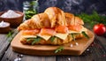 Croissant sandwich with cheese, salmon and arugula on wooden board, table background with ingredients, close up Royalty Free Stock Photo