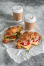 Croissant sandwich and cup coffee on gray concrete background. Croissants with ham and fresh vegetables. Side view, selective Royalty Free Stock Photo