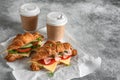 Croissant sandwich with a cup of coffee, gray grunge background. Croissants with ham and fresh vegetables. Side view Royalty Free Stock Photo