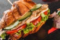 Croissant sandwich with fillet grilled chicken, fresh vegetables, cheese and greens on black shale board over black background Royalty Free Stock Photo