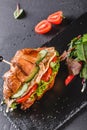 Croissant sandwich with fillet grilled chicken, fresh vegetables, cheese and greens on black shale board over black stone Royalty Free Stock Photo