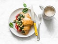 Croissant sandwich with scramble spinach eggs, tomato and cream cheese and coffee on a light background, top view