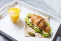 Croissant sandwich with tuna, hard boiled egg, salad and cucumber on white tray. Glass of orange juice. Breakfast Royalty Free Stock Photo