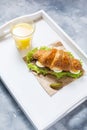 Croissant sandwich with tuna, hard boiled egg, salad and cucumber on white tray. Glass of orange juice. Breakfast Royalty Free Stock Photo