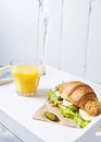 Croissant sandwich with tuna, hard boiled egg, salad and cucumber on white tray. Glass of orange juice. Breakfast concept Royalty Free Stock Photo