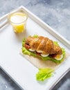 Croissant sandwich with tuna, hard boiled egg, salad and sun-dried tomatoes on white tray. Glass of orange juice. Royalty Free Stock Photo