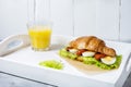 Croissant sandwich with tuna, hard boiled egg, salad and sun-dried tomatoes on white tray. Glass of orange juice. Breakfast concep Royalty Free Stock Photo