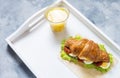 Croissant sandwich with tuna, hard boiled egg, salad and sun-dried tomatoes on white tray. Glass of orange juice. Breakfast concep Royalty Free Stock Photo