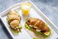 Croissant sandwich with tuna, hard boiled egg, salad and sun-dried tomatoes on white tray. Glass of orange juice. Royalty Free Stock Photo